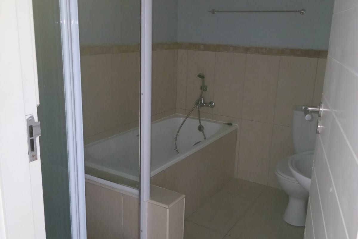 A functional bathroom featuring a built-in bathtub with shower attachment, a toilet, and tiled flooring and wall surrounds.