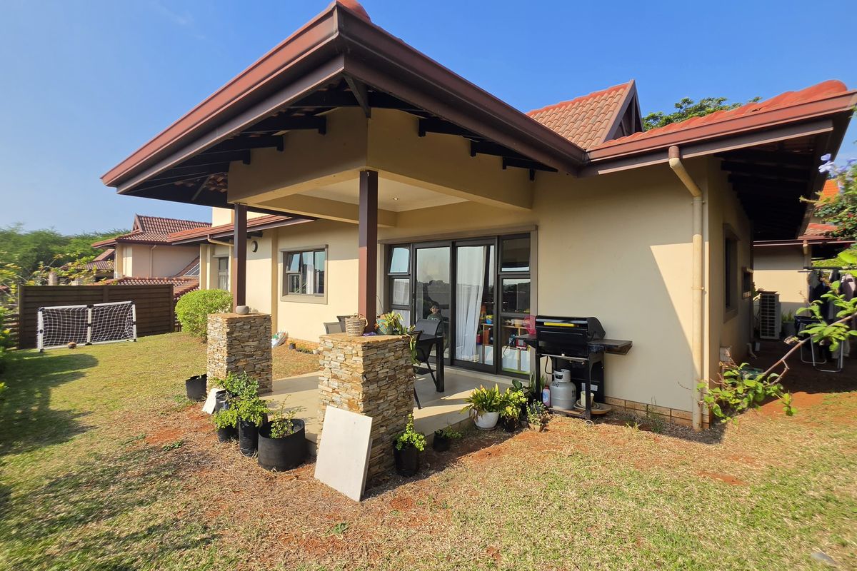 Rear view of the townhouse featuring a covered patio with stone-clad pillars, sliding glass doors, and a private garden area.