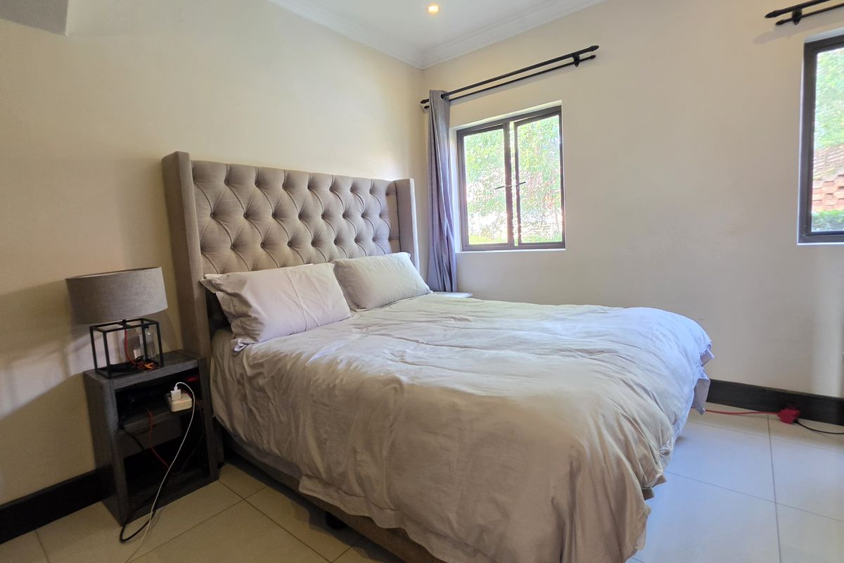 A well-lit bedroom featuring tiled flooring, neutral wall finishes, and windows with curtain rods, providing a comfortable and functional living space.