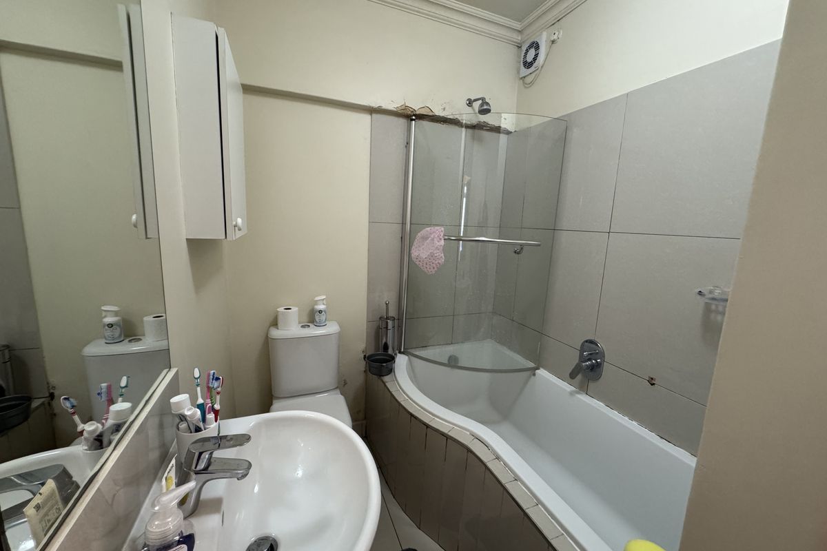 A compact bathroom featuring a curved bathtub with a glass shower screen, a wall-mounted basin, and a toilet.