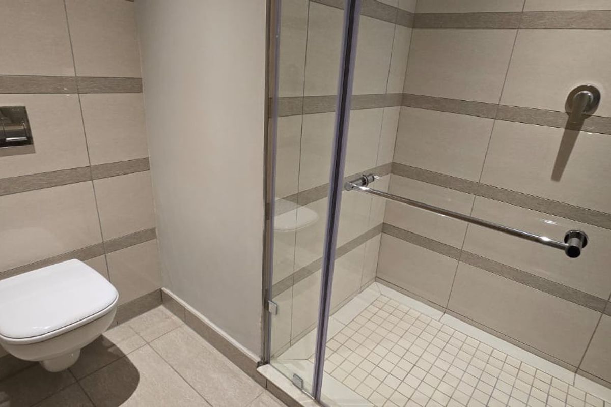 Modern bathroom featuring a wall-mounted toilet and a walk-in shower with glass enclosure and tiled walls.