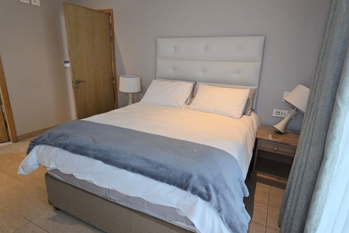 A well-maintained bedroom featuring tiled flooring, neutral wall finishes, and two wooden doors leading to adjacent spaces.
