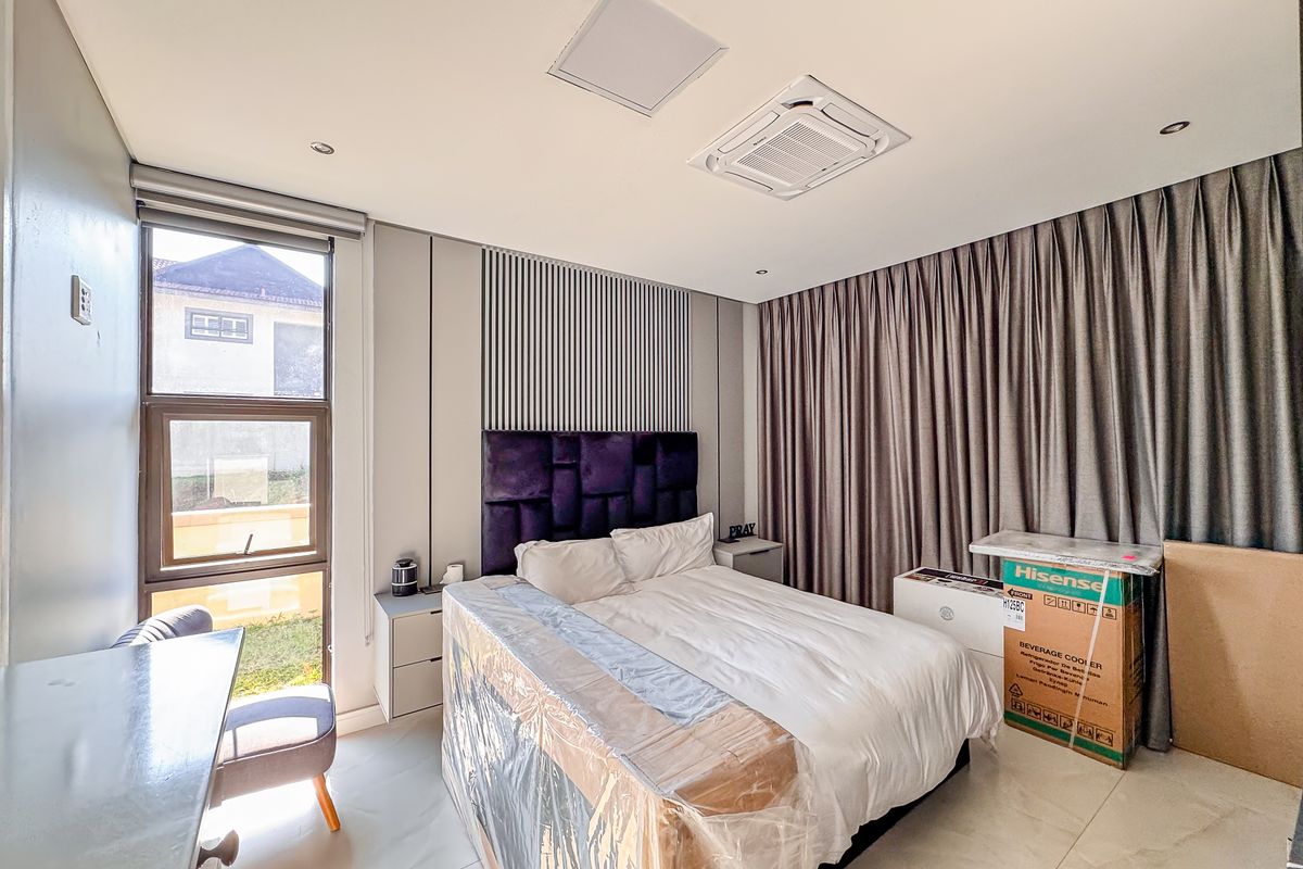 A modern bedroom featuring a built-in headboard, recessed ceiling lighting, and a ducted air conditioning unit.