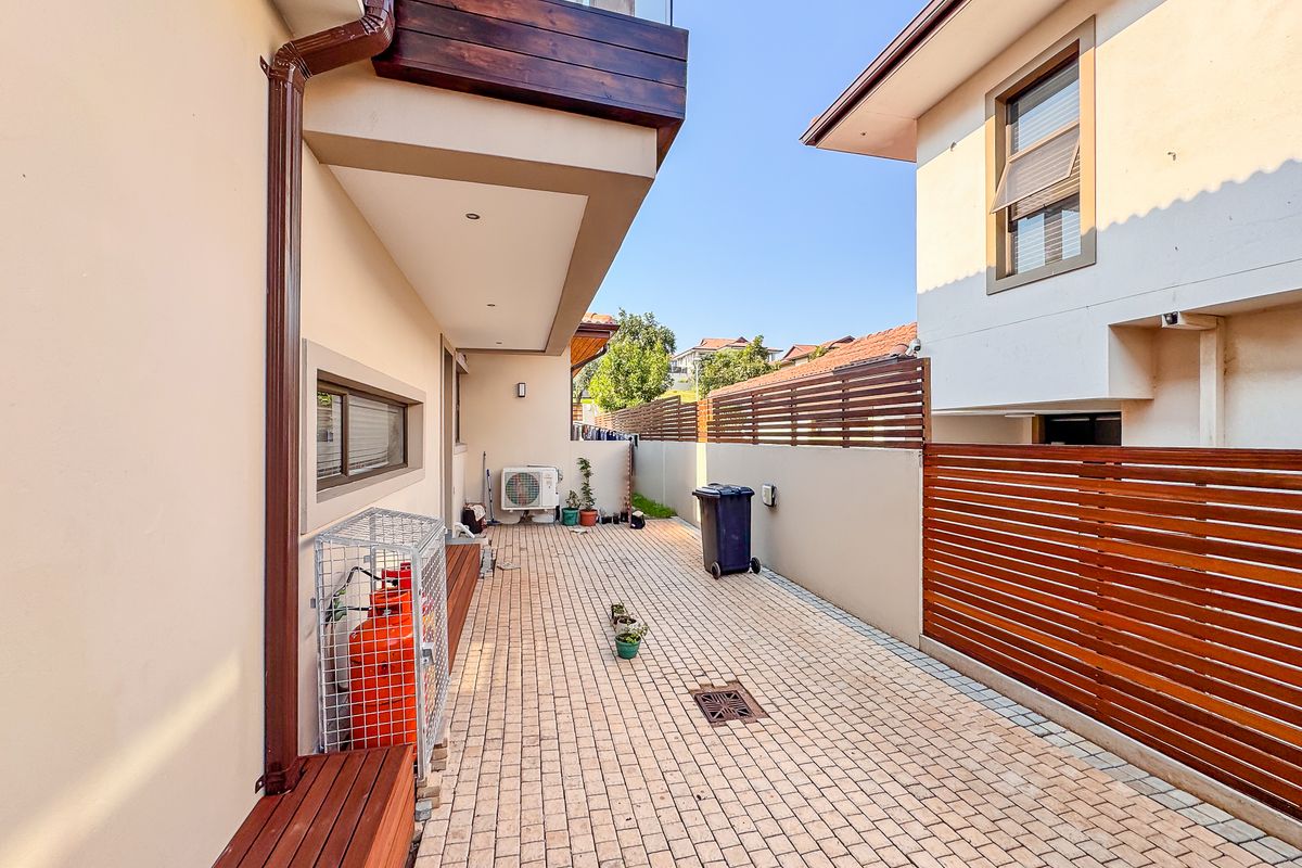 A paved side exterior area featuring a timber-slatted privacy screen, downpipes, and an integrated outdoor air conditioning unit.