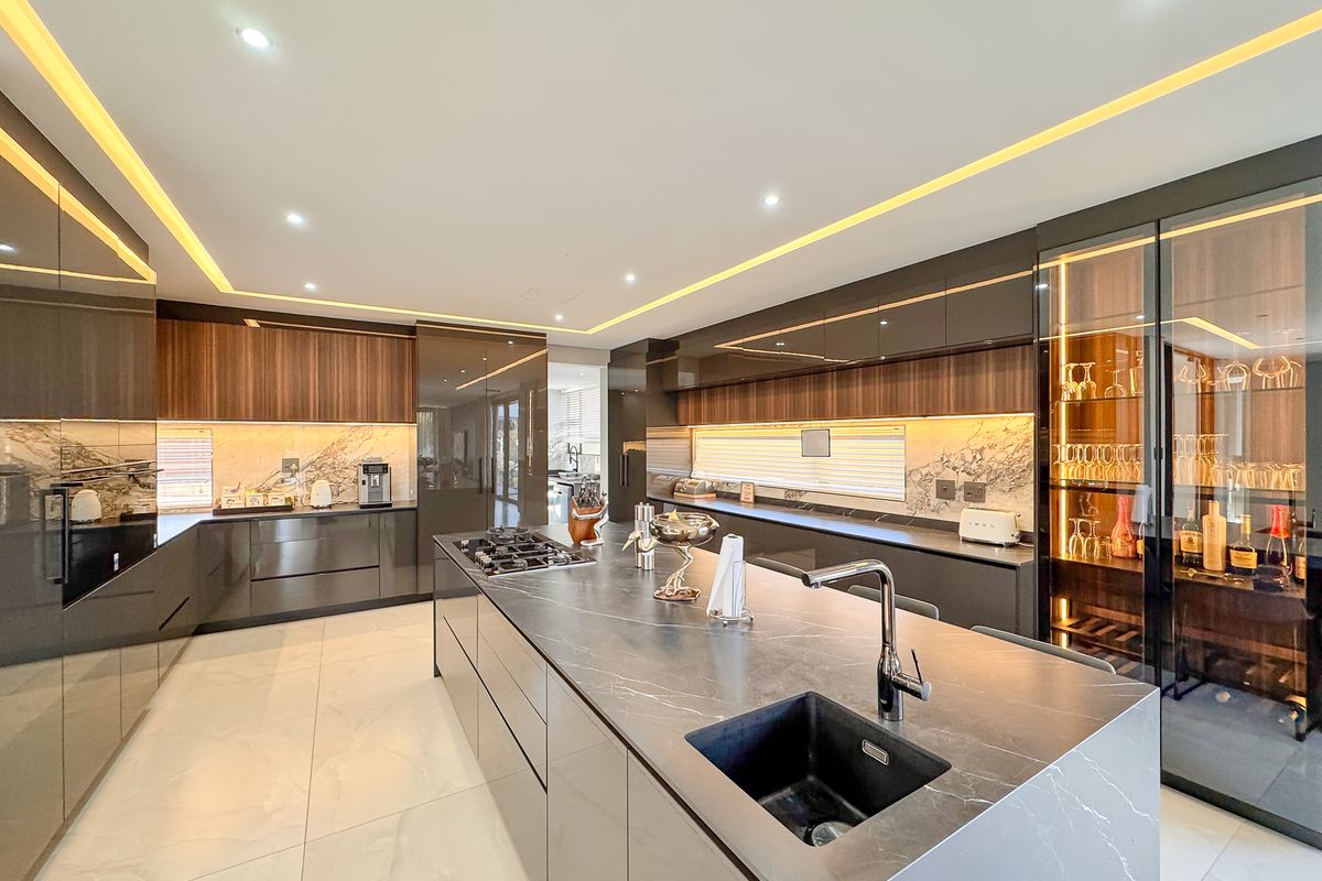 Modern luxury kitchen featuring a large central island with stone countertop, integrated sink, gas hob, high-end cabinetry, and ambient recessed lighting.