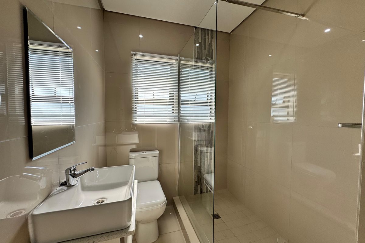 Modern bathroom featuring a glass-enclosed walk-in shower, contemporary basin with vanity, and neutral floor-to-ceiling tiling.