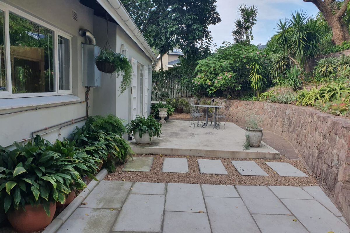 A paved rear patio area featuring a stone retaining wall, established garden beds, and direct access to the home's exterior.