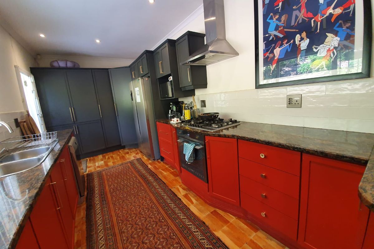 A kitchen featuring a mix of dark and red cabinetry, granite countertops, a stainless steel extractor fan, and a built-in oven and gas hob.