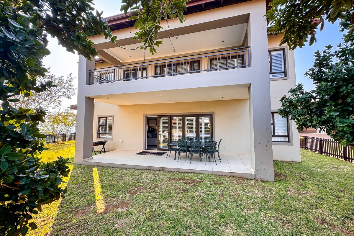 Rear view of the townhouse featuring a covered patio, upper-level balcony with metal railings, and a private garden area.