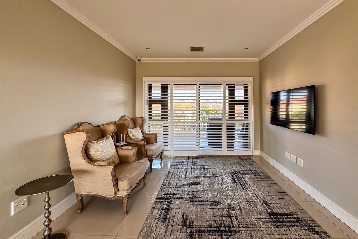 A well-maintained living room featuring tiled flooring, recessed ceiling lighting, crown molding, and large sliding doors with integrated plantation shutters.