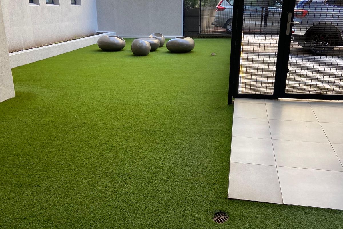 A private courtyard area featuring low-maintenance artificial turf, tiled patio sections, and secure metal gate access.