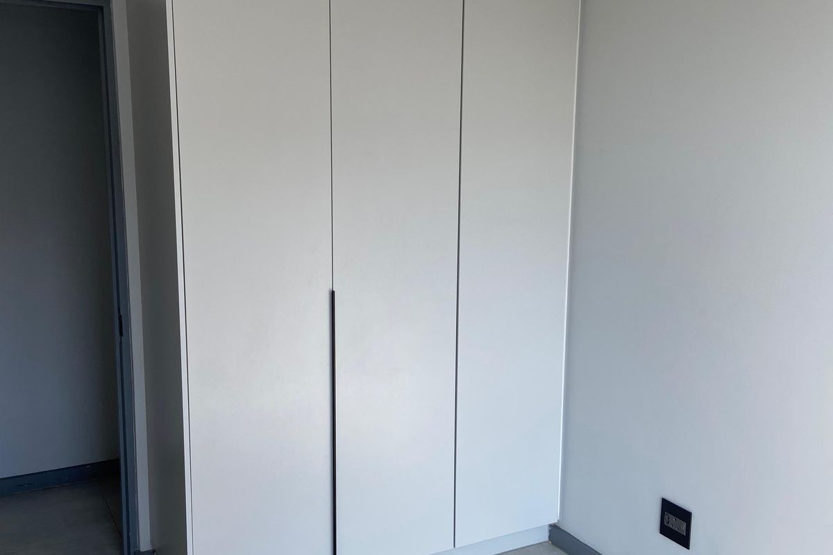 A modern bedroom featuring built-in floor-to-ceiling cabinetry, neutral grey floor tiles, and recessed ceiling lighting.
