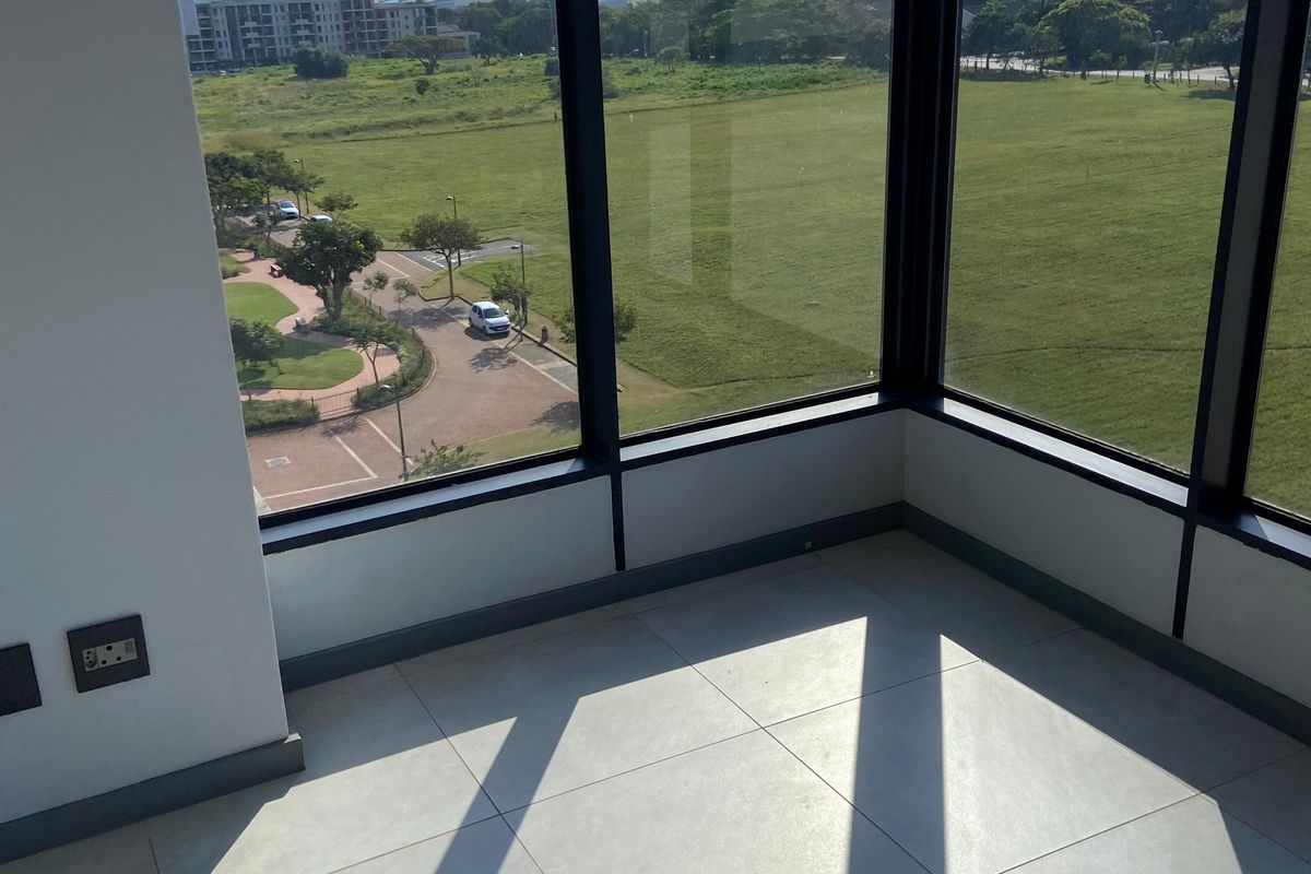 A bright, modern corner room featuring floor-to-ceiling windows with expansive views of the surrounding landscape and green space.