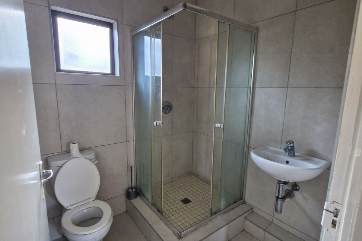 A compact bathroom featuring floor-to-ceiling tiling, a corner glass shower enclosure, a wall-mounted basin, and a standard toilet.