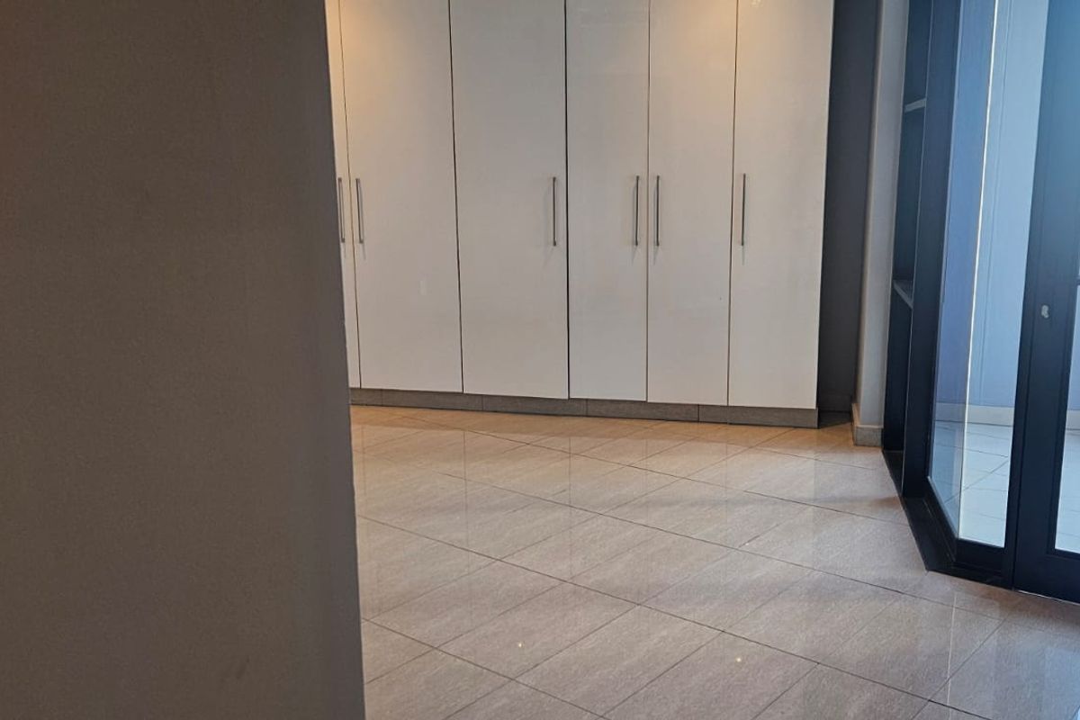A bright bedroom featuring built-in floor-to-ceiling white cabinetry, tiled flooring, and direct access to a private balcony through a glass door.