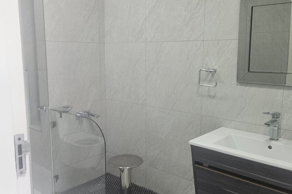 Modern bathroom featuring a vanity with integrated basin, glass-enclosed shower, and contemporary grey wall tiling.