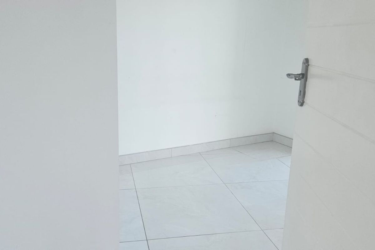 A view into an empty, neutrally finished room featuring light-colored floor tiles and a white door.