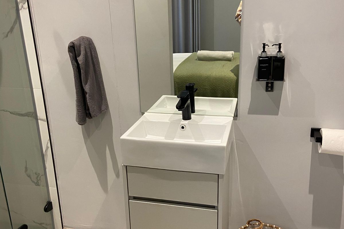 Modern bathroom featuring a wall-mounted vanity with a square basin, black faucet, and a glass-enclosed shower with marble-look tiling.
