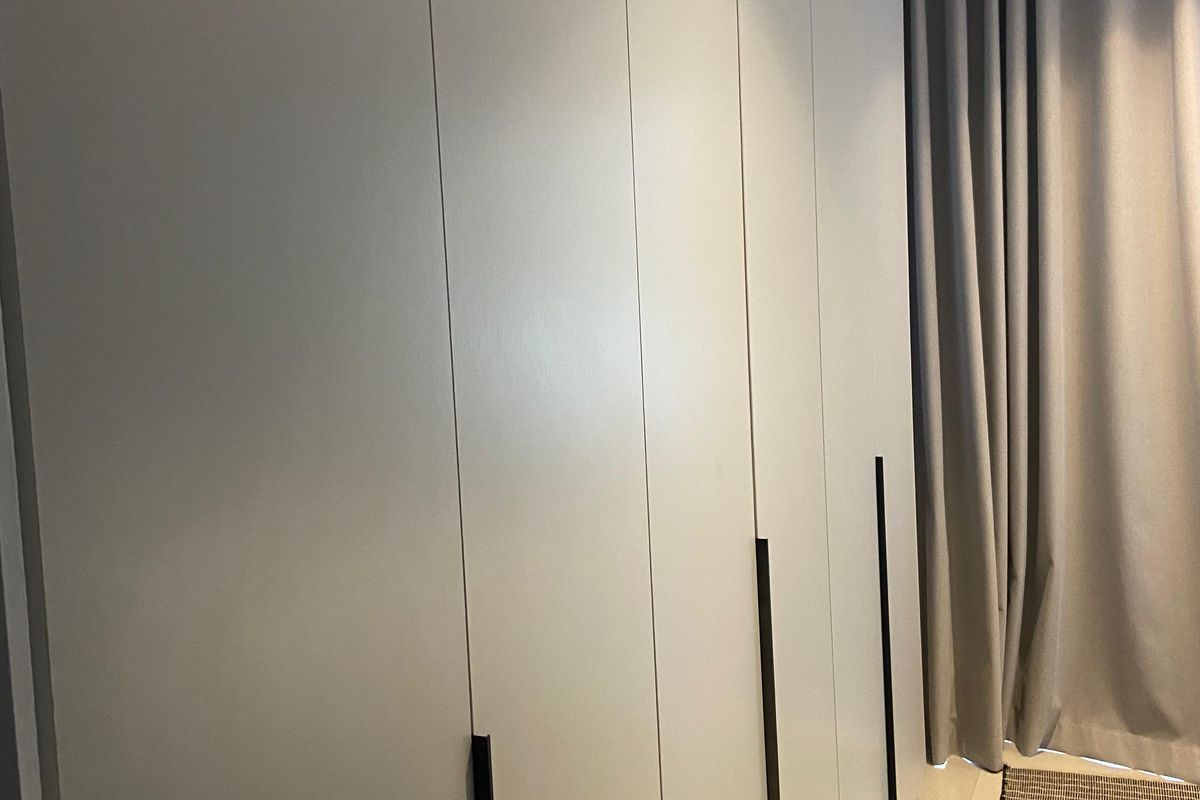 A modern bedroom featuring floor-to-ceiling built-in wardrobes with sleek matte grey finish and minimalist black handles.