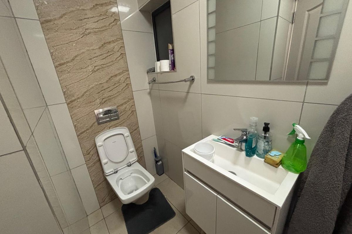 Modern bathroom featuring a wall-mounted toilet with a feature tile backsplash, a vanity cabinet with integrated basin, and a wall-mounted mirror.