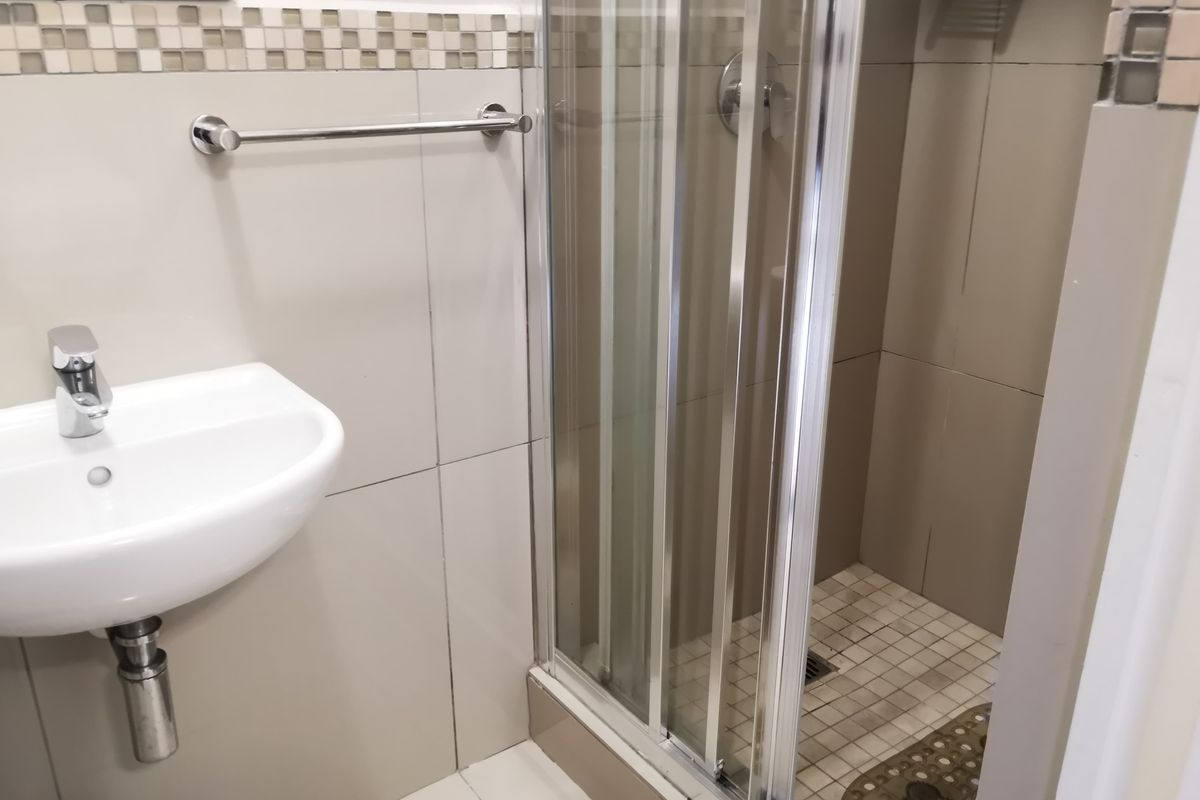 A compact bathroom featuring a wall-mounted basin, chrome fixtures, and a glass-enclosed shower with neutral wall tiling.