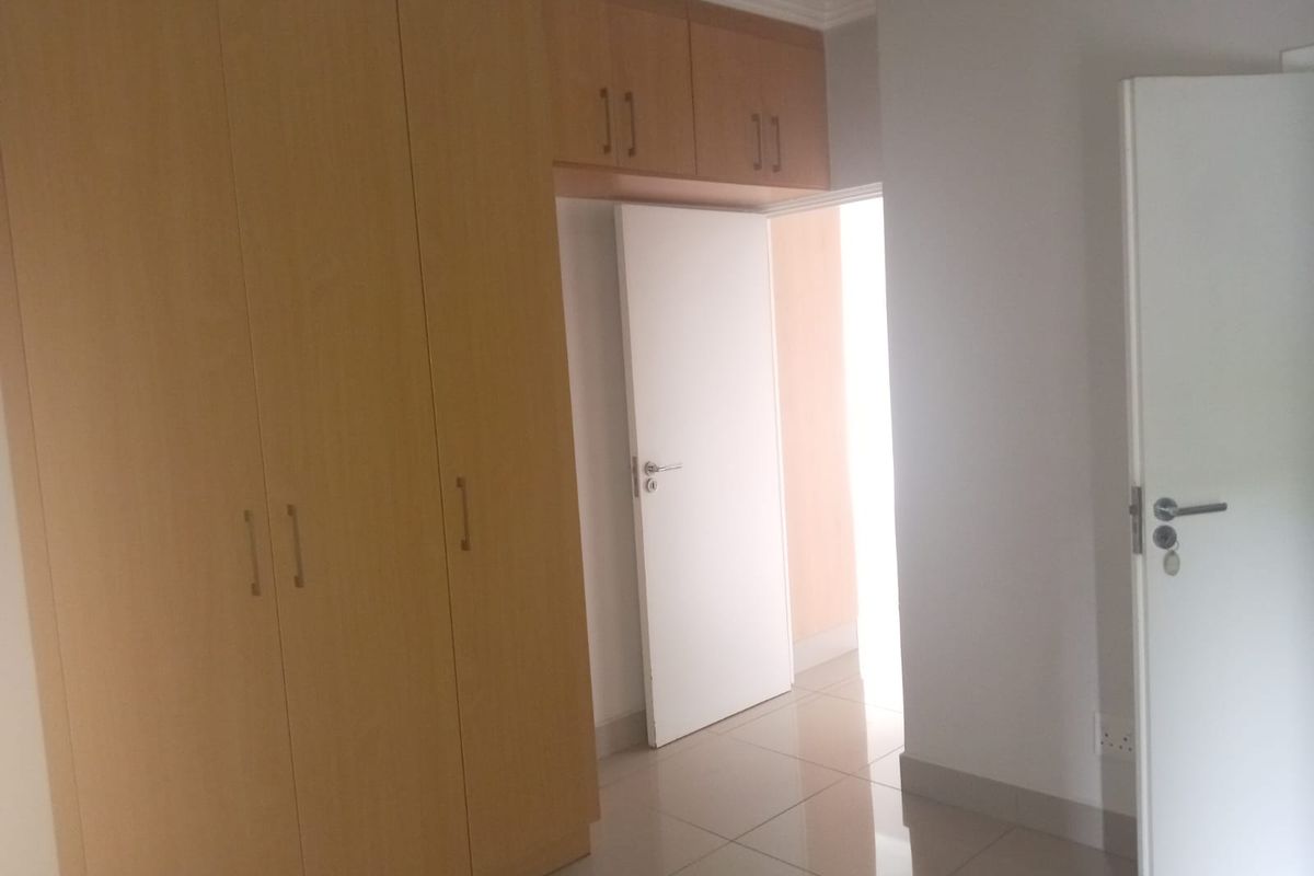 A bedroom featuring built-in wooden cupboards with overhead storage and tiled flooring, leading to an adjacent room.