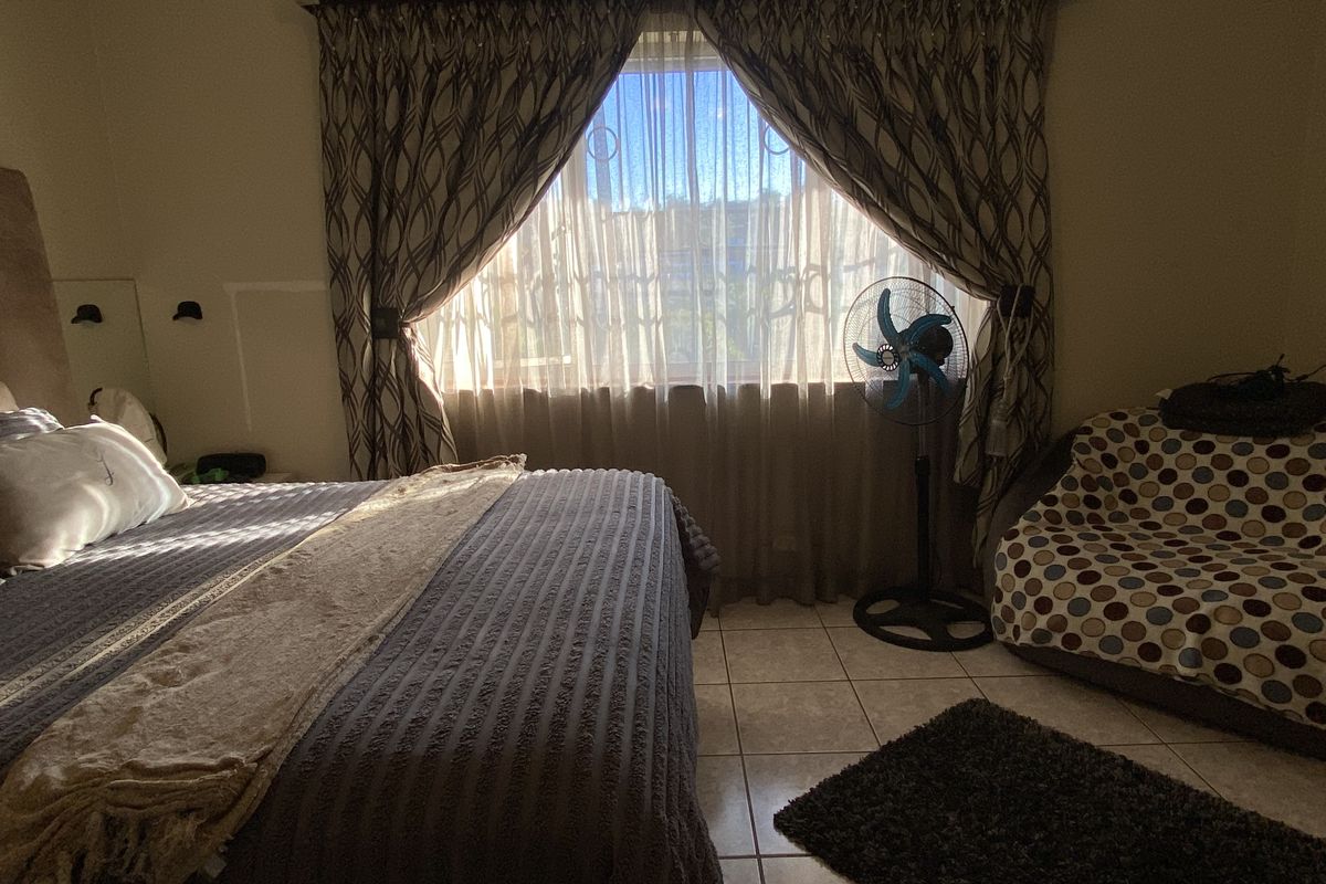 A bedroom featuring tiled flooring, a window with curtain treatments, and built-in wall-mounted lighting fixtures.