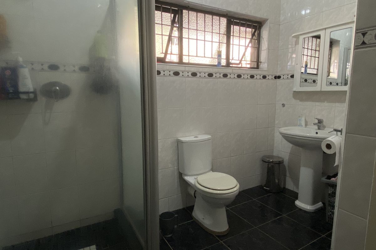 A functional bathroom featuring a glass-enclosed shower, pedestal basin, and toilet, finished with tiled walls and flooring.