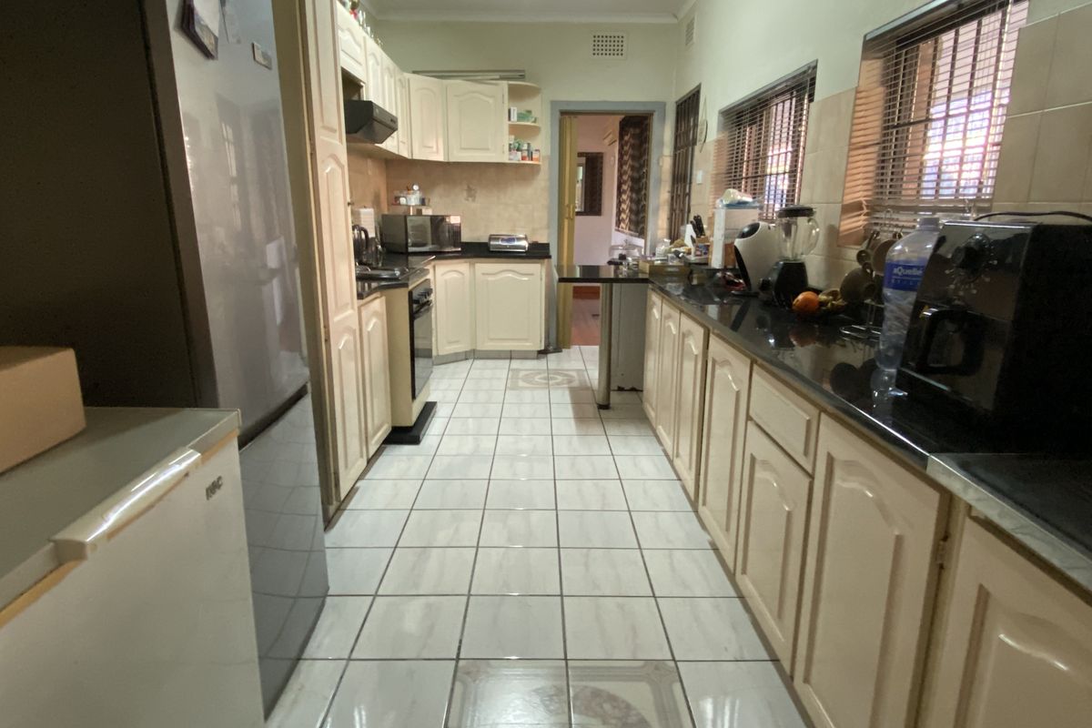 A functional galley-style kitchen featuring light-toned cabinetry, dark granite countertops, and tiled flooring with a central decorative inlay.