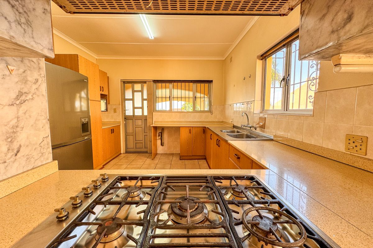 A functional kitchen featuring wooden cabinetry, stone-look countertops, a built-in gas hob, and a double stainless steel sink with natural light.