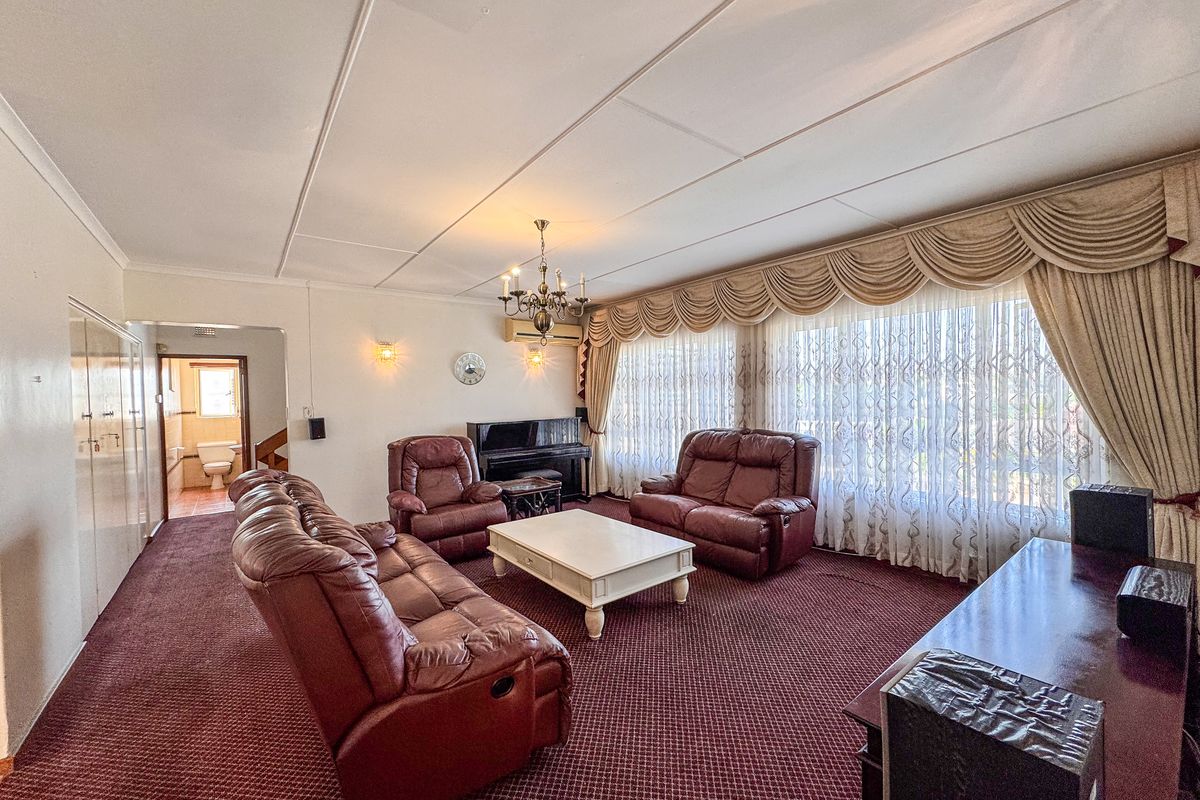 Spacious living room featuring large windows with classic drapery, wall-mounted lighting, and direct access to an adjacent bathroom area.