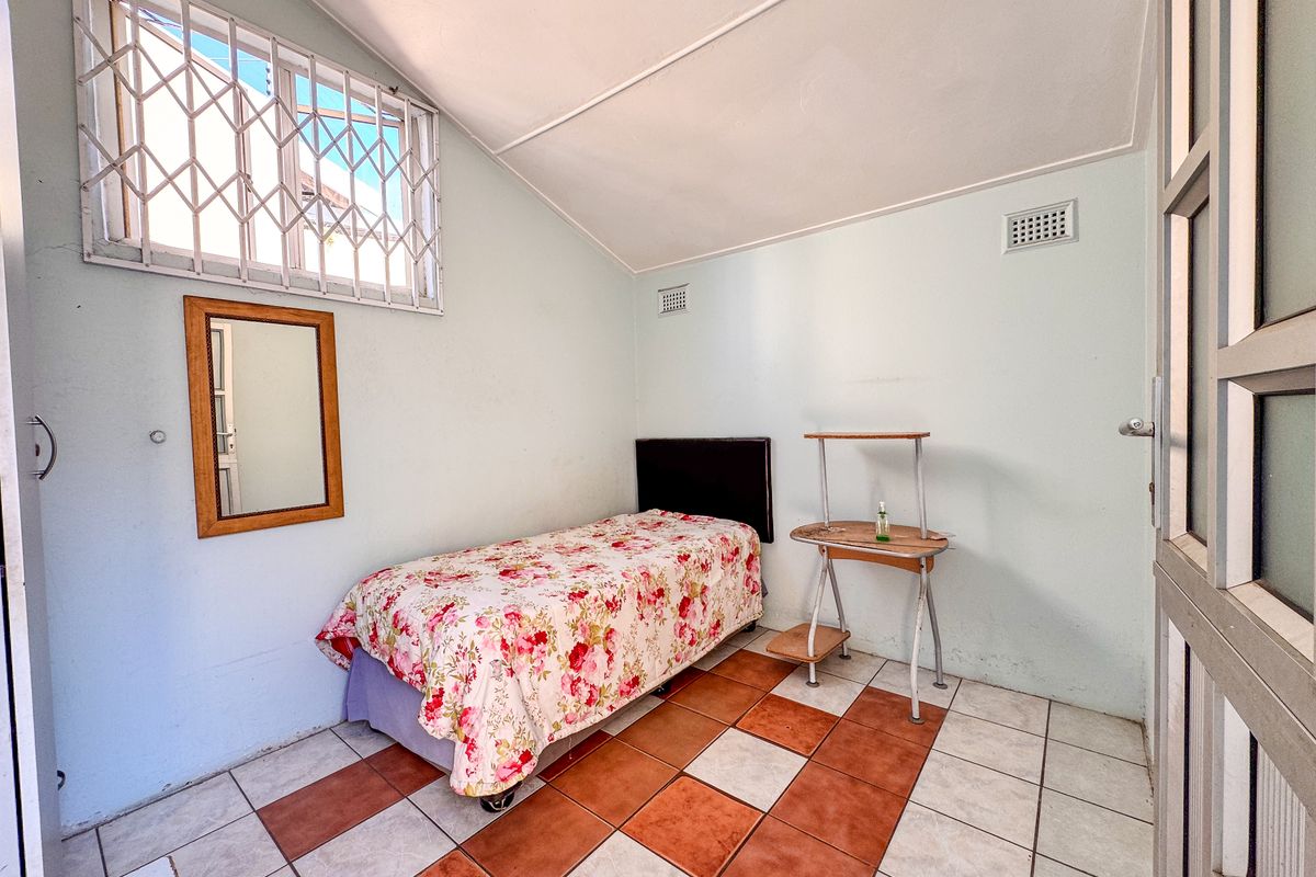 A simple bedroom featuring tiled flooring, a security gate on the window, and a sloped ceiling.