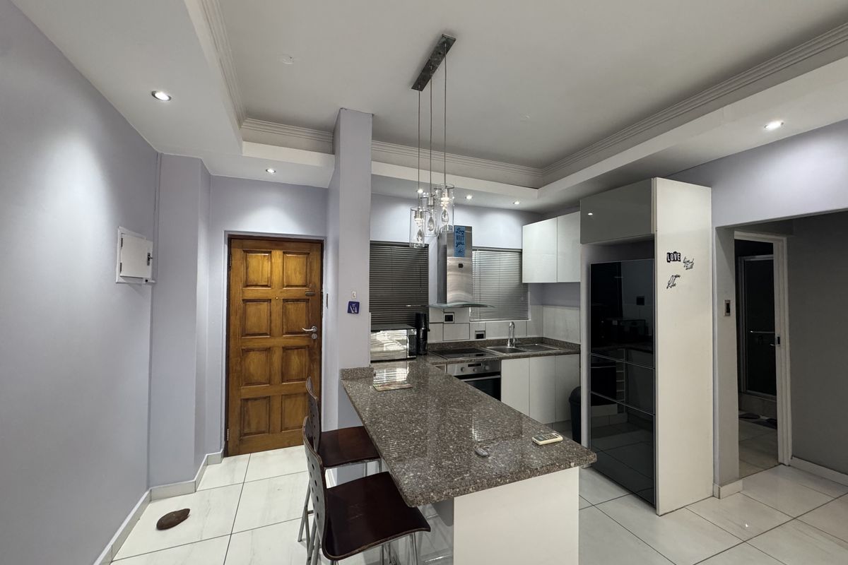 Modern kitchen featuring granite countertops, a breakfast bar, built-in oven, extractor fan, and sleek cabinetry with tiled flooring throughout.