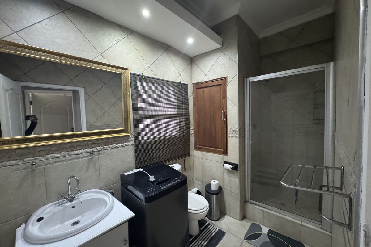 A functional bathroom featuring a glass-enclosed shower, vanity basin, and integrated laundry space with tiled walls and recessed lighting.