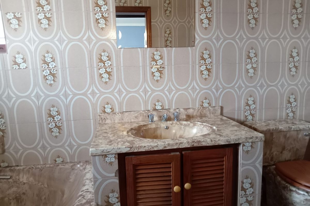 A dated bathroom featuring patterned wall tiles, a built-in vanity with a marble-effect countertop, and a matching integrated bathtub.