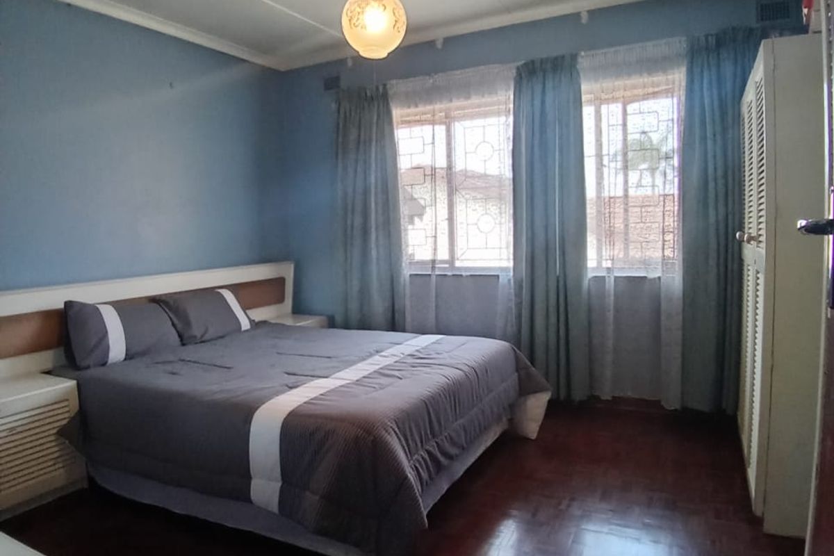 A bedroom featuring dark parquet flooring, built-in cupboards, and large windows with security bars, providing a functional and well-lit living space.