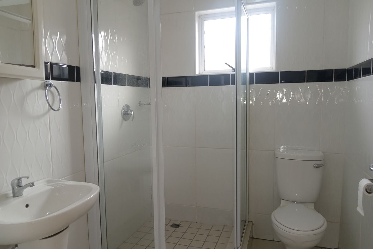 A functional bathroom featuring a glass-enclosed shower, pedestal basin, and standard toilet with white wall tiling and a decorative black accent border.