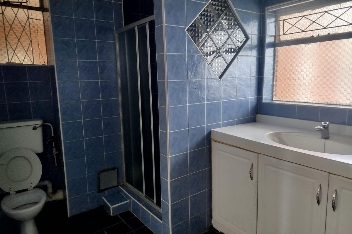 A dated bathroom featuring blue wall tiles, a shower enclosure, a vanity unit with basin, and a toilet, with a glass block feature window.