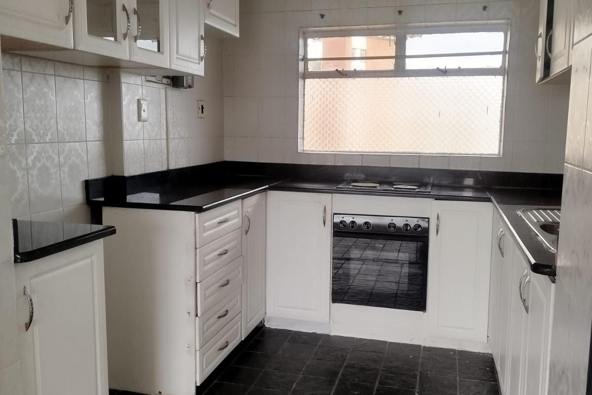 A functional kitchen featuring white cabinetry, black granite countertops, integrated oven and hob, and tiled finishes throughout.