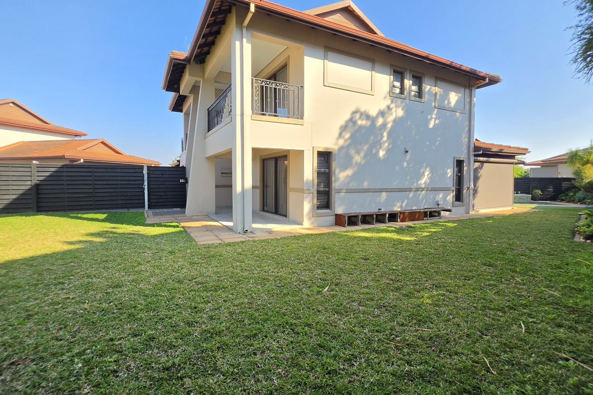 A view of the townhouse rear elevation featuring a covered patio, upper-level balcony with metal railing, and a spacious private garden area.