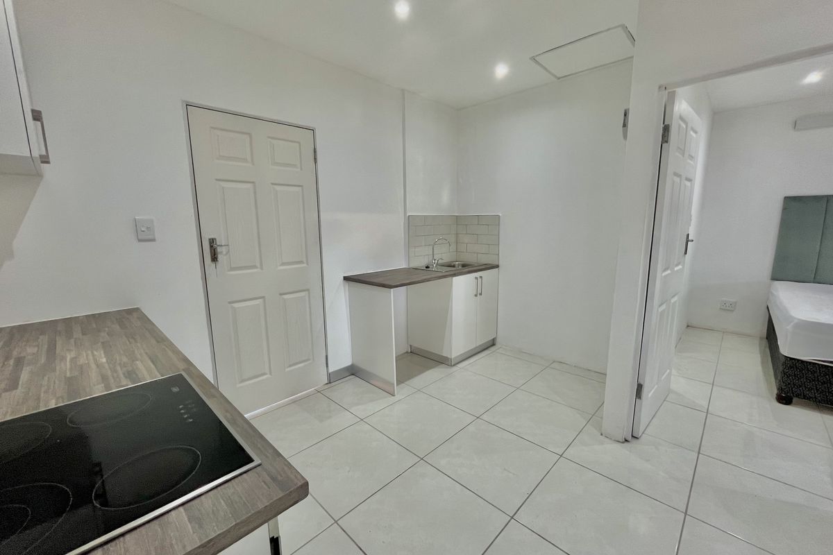 A compact kitchen area featuring a built-in hob, laminate countertops, and a small sink unit with tiled splashback, finished with neutral floor tiles.