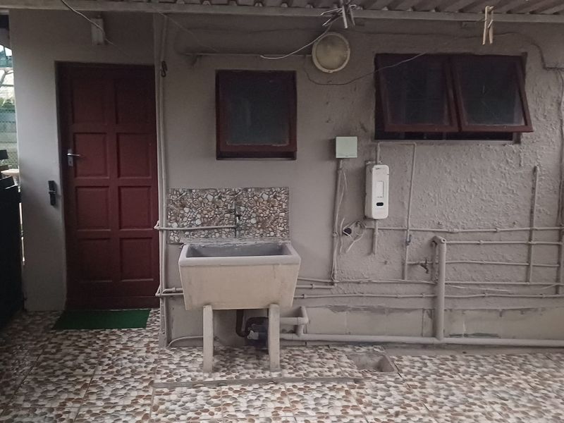 Outdoor laundry area featuring a concrete sink, tiled flooring, and exposed utility connections under a corrugated roof structure.