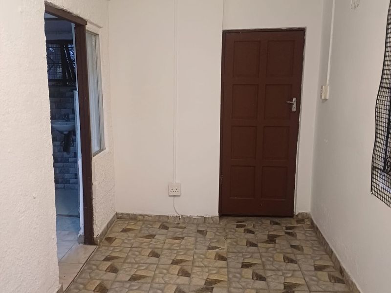 A vacant hallway featuring tiled flooring and a timber door, providing access to an adjacent room with visible sink fixtures.