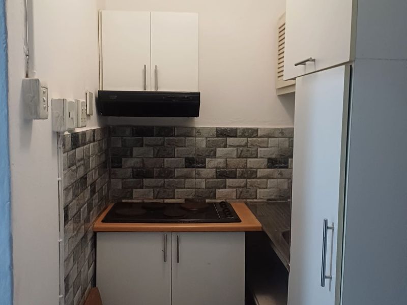 Compact kitchen featuring white built-in cabinetry, an electric hob with extractor fan, and a decorative tiled backsplash.