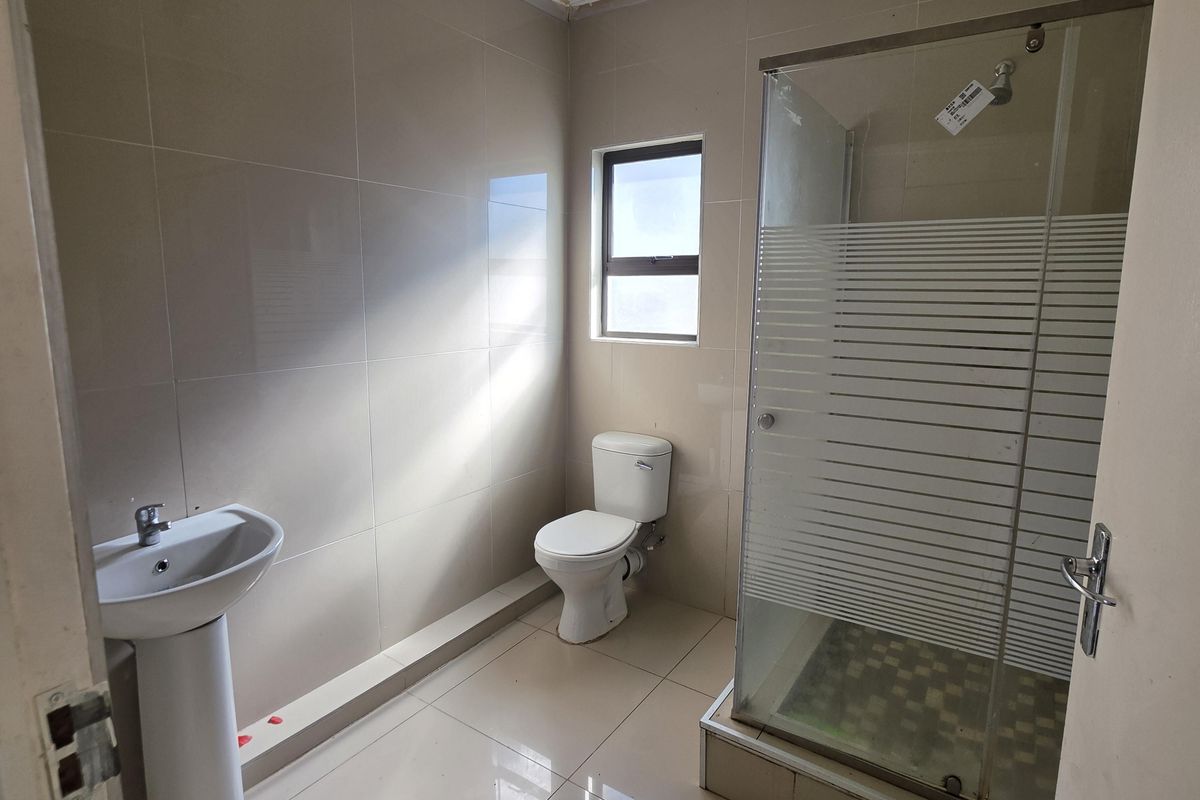 A functional bathroom featuring a glass-enclosed shower, pedestal basin, and toilet with neutral wall and floor tiling.