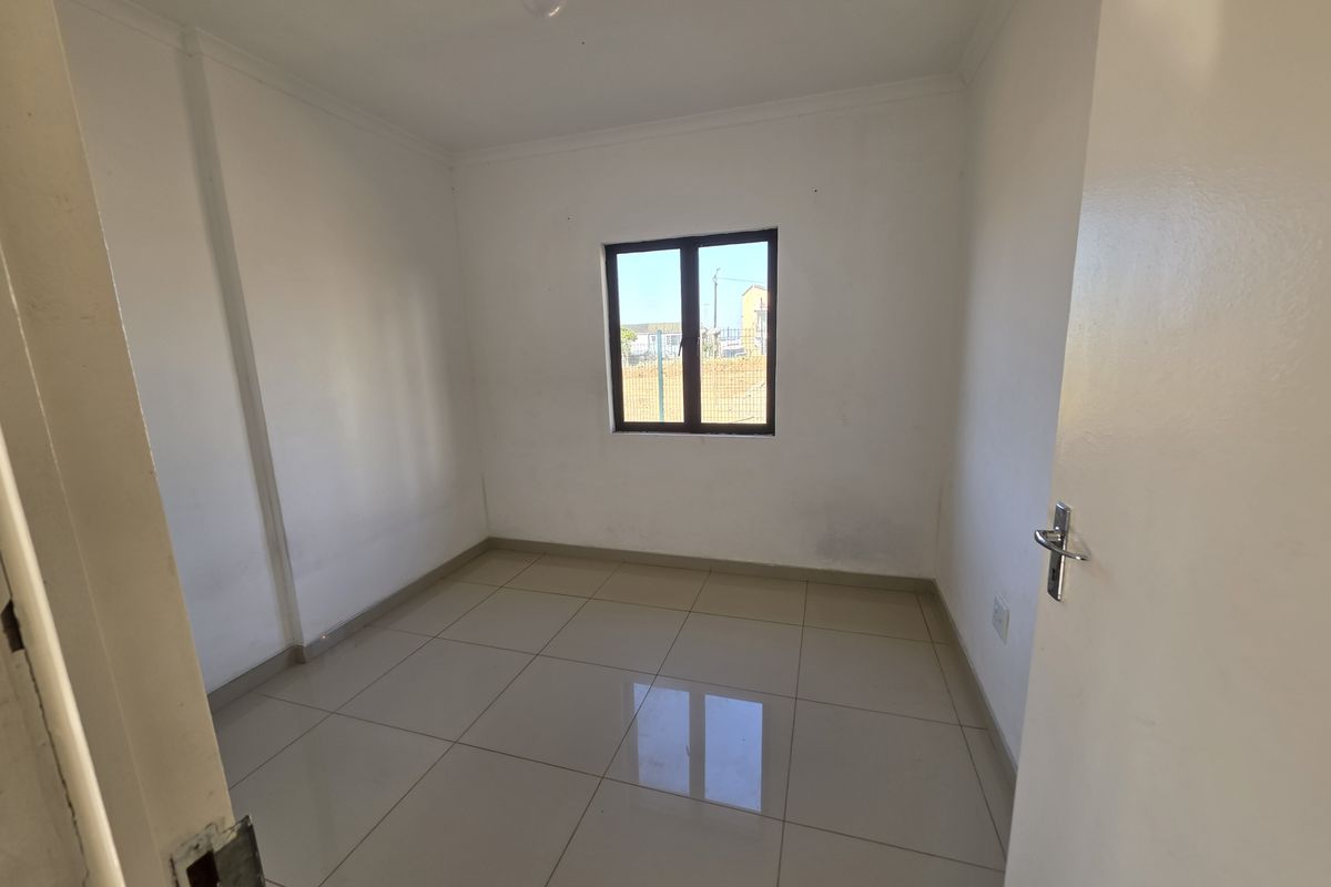 A clean, empty bedroom featuring neutral tiled flooring, white walls, and a single window providing natural light.