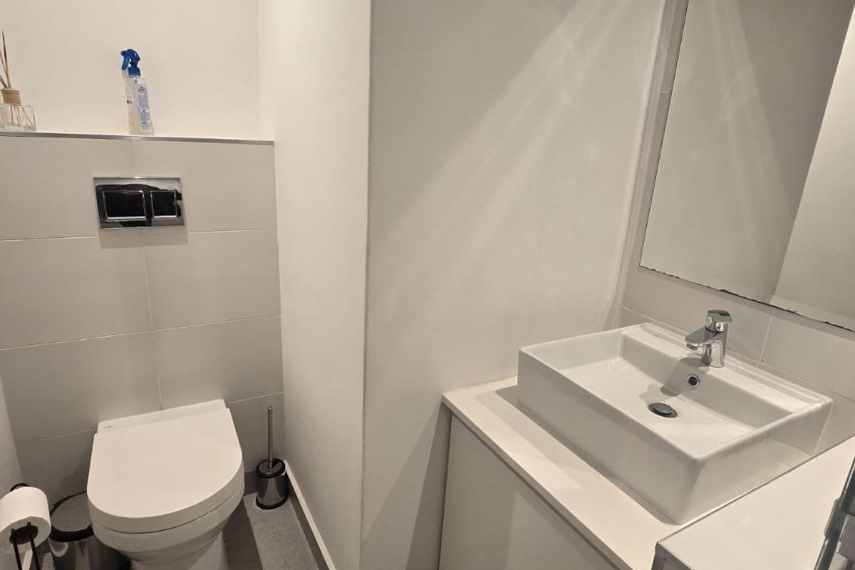 A modern bathroom featuring a wall-mounted toilet with a concealed cistern, a vessel sink vanity, and a large wall mirror.