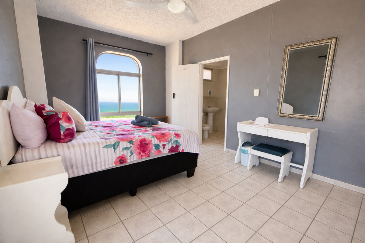 A bedroom featuring tiled flooring, an arched window with ocean views, and an en-suite bathroom with a pedestal basin.
