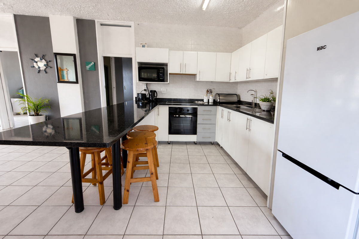 A functional kitchen featuring white cabinetry, a black granite breakfast bar, built-in oven, and tiled flooring in an open-plan layout.