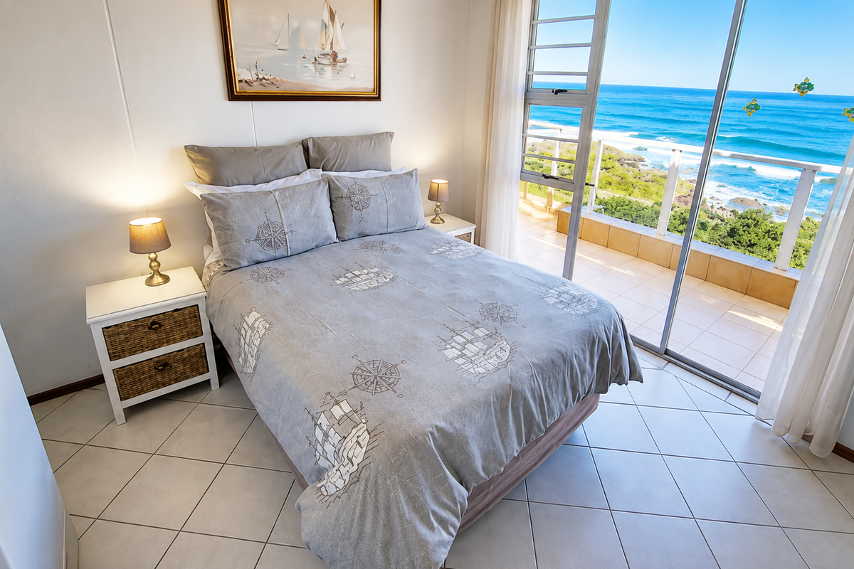 A bright bedroom featuring tiled flooring and large sliding glass doors that open onto a balcony with expansive ocean views.